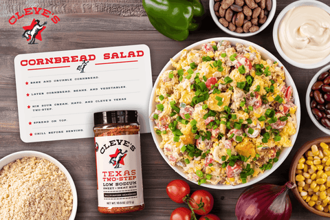 Bowl of Cleve's cornbread salad with corn, tomatoes, beans, and green onions, beside crumbled cornbread and a bottle of Texas Two-Step seasoning