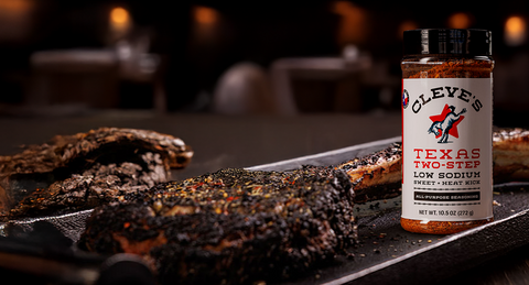 Cleve's Texas Two-Step Low Sodium Sweet Heat seasoning bottle with grilled meat on a dark background